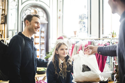 Family receiving shopping bag from salesman at checkout counter in boutique