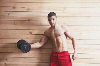 Shirtless man exercising against wooden wall