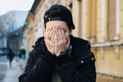 Young woman covering face with hands on footpath