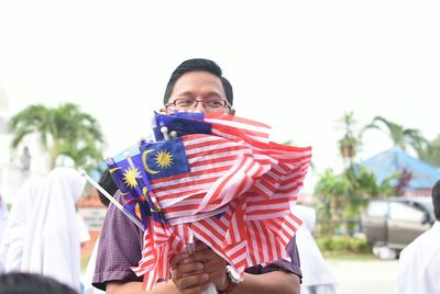Smiling man holding malaysian flags against clear sky