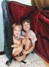 Portrait of smiling siblings sitting in suitcase at home