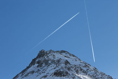 Low angle view of vapor trail and the european alps against clear blue sky