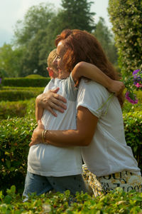 Happy mother embracing son while standing amidst plants in park