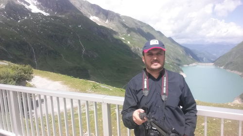 Portrait of young man standing on railing against mountains