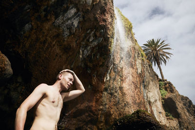 Young man enjoying under waterfall from cliff. rocky coast of tenerife, canary islands, spain