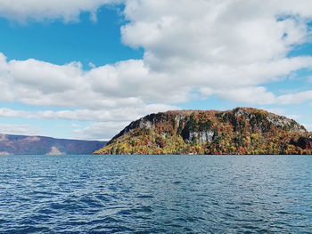 Scenic view of sea by mountain against sky