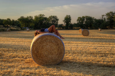 Woman enjoying hay bales on field against sky in tuscany