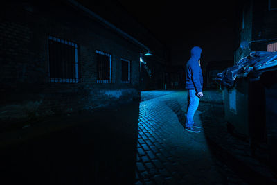Side view of man standing on illuminated footpath at night