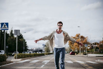 Young man with arms outstretched against sky