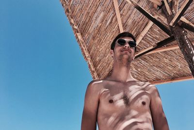 Low angle view of shirtless man against clear blue sky