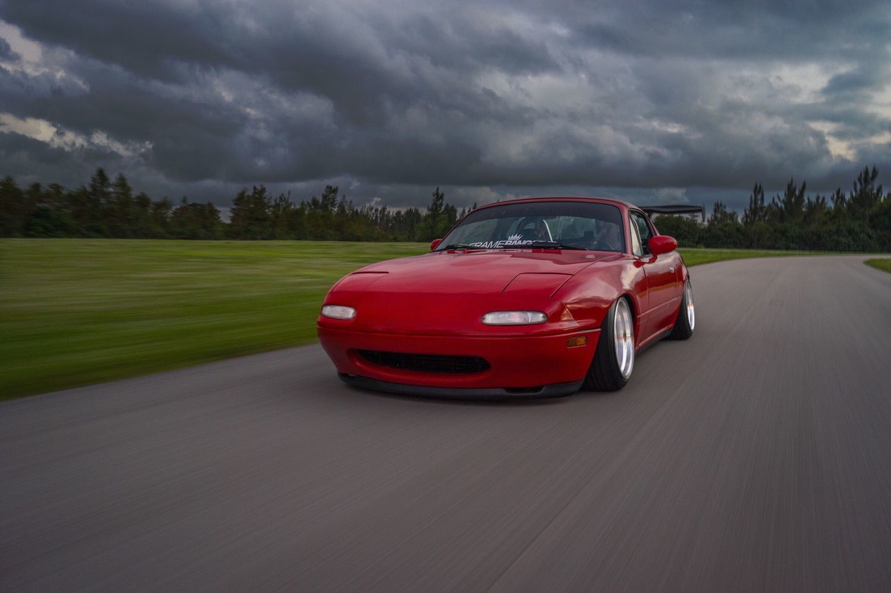 transportation, sky, road, cloud - sky, red, cloudy, land vehicle, mode of transport, car, field, landscape, grass, road marking, the way forward, cloud, tree, country road, overcast, street, weather