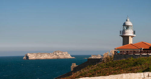 Lighthouse by sea against clear sky