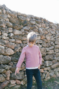Boy pointing down while standing against stone wall
