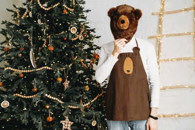 Funny man in front of christmas tree ready for celebration with gifts in bear mask and costume