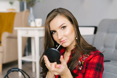 Young caucasian woman in a red plaid shirt and skirt does her makeup, paints her lips with glitter