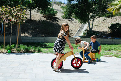 Little girl stands over a wooden push bike and looks at camera