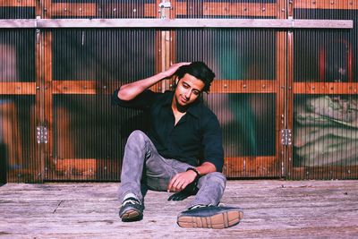 Full length of happy young man sitting by wall