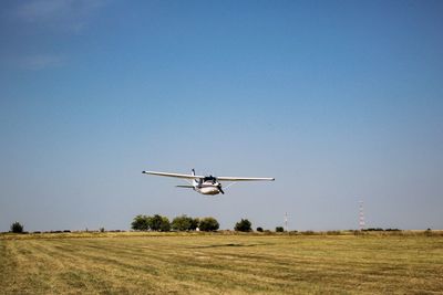 Airplane flying over field against clear sky