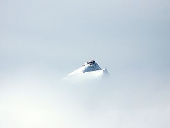 House on top of snowcapped mountain against clear sky during foggy weather