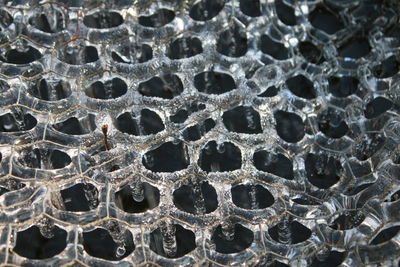 Close up of frozen ice in icicles and hexagon patterns on metal wire cover on pond in winter freeze