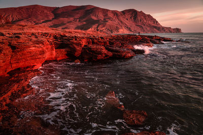 Rock formation in sea against sky during sunset