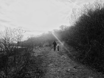 Rear view of father and daughter walking on pathway against sky