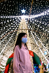 Portrait of woman standing against illuminated wall at christmas night