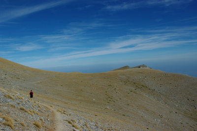 Man walking on mountain trail against blue sky