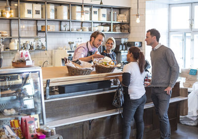 Mid adult owner attending customers at counter in restaurant