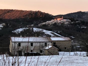 Snow covered houses by buildings against sky