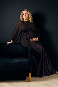 Portrait of pregnant woman sitting on sofa against black background