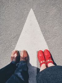 Low section of man and woman wearing shoes standing on road with arrow sign