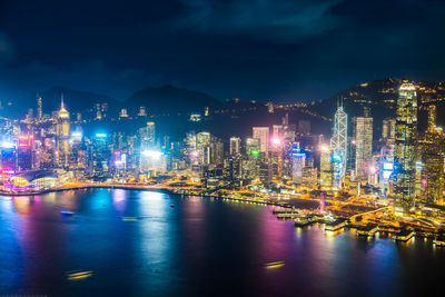 Illuminated buildings by sea against sky at night