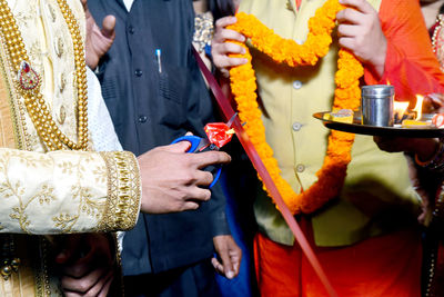 Midsection of groom cutting ribbon by men during wedding ceremony