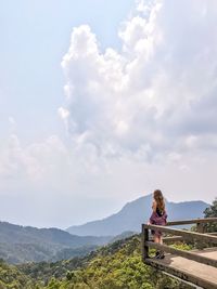 Woman standing at observation point on mountain road against sky