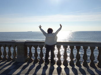 Rear view of woman with arms raised standing against sea