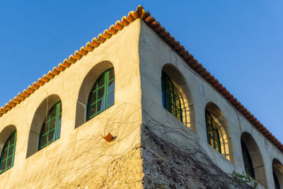 Building corner with green arched windows and tiled roof at sunset