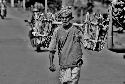 Senior man carrying firewood while walking on road