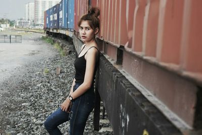 Side view portrait of young woman standing by freight train