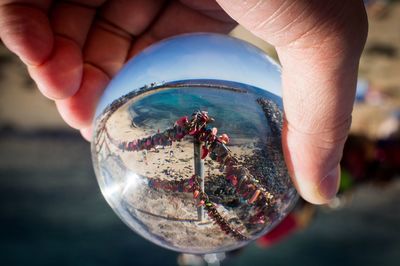 Close-up of hand holding crystal ball against sea