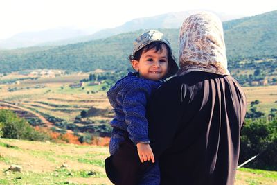 Portrait of son carried by mother on field