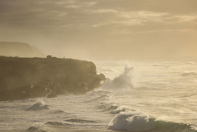 Waves splashing on shore against sky