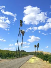 Road passing through field against cloudy sky