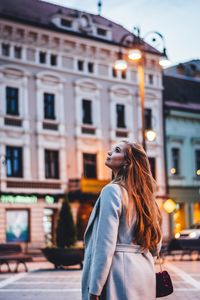 Side view of young woman standing against building in city