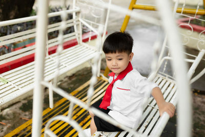 Cute boy playing while sitting on swing outdoors