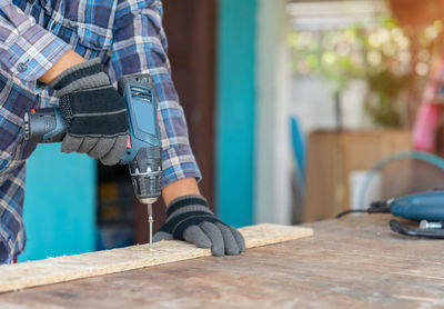 Carpenter use cordless screwdriver to driving screw nail into wood sheet on the table in workshop