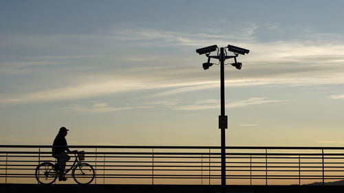 Silhouette man riding bicycle on street against sky