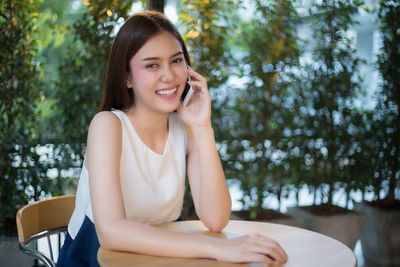 Portrait of smiling young woman using phone while sitting at sidewalk cafe