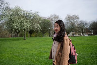 Young woman standing on grass against trees