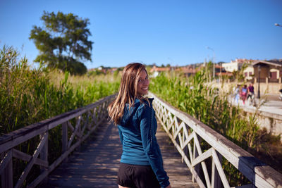 Woman standing on railing against blue sky